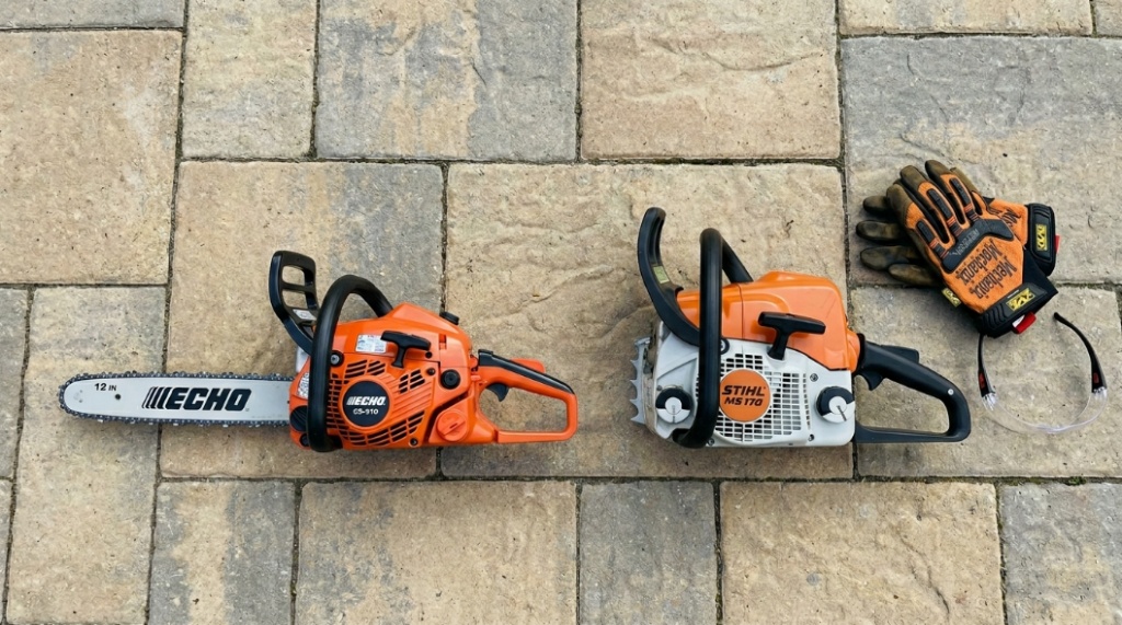A 12-inch and 16-inch gas chainsaw side by side on a patio next to safety gloves.