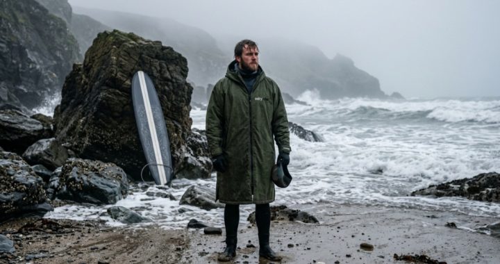 Surfer wearing a hooded windproof surf poncho on a misty cold water beach.
